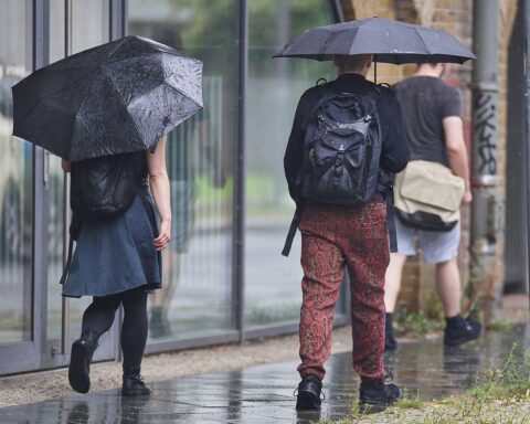 Personen mit Regenschirmen unter grauem Himmel, symbolisieren nassen und trüben Wetterbericht für Hamburg.