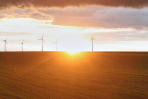 Windräder im Sonnenlicht, umgeben von blauen Himmel und aufgelockerten Wolken.