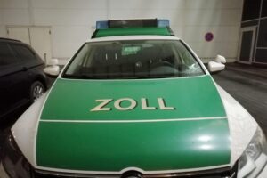 Zollbeamte bei einer Kontrolle, Akten, Zahlen zur Schwarzarbeit und symbolische Darstellungen der Ermittlungen.