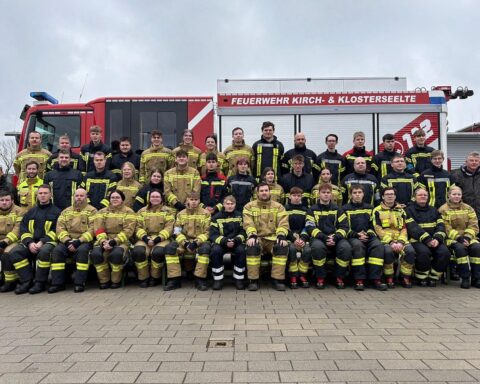 Feuerwehrleute feiern Abschluss ihrer Grundausbildung, stolz in Uniform mit Zertifikaten und Feuerwehrfahrzeug.