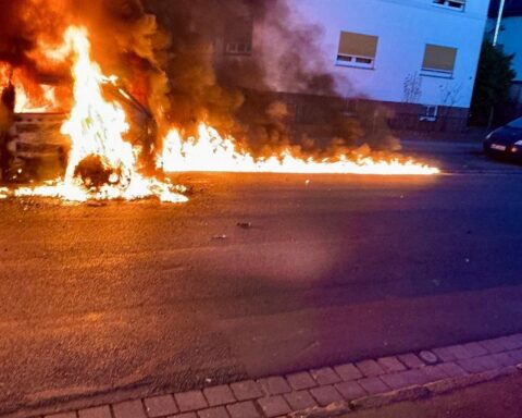 Ein brennendes Auto, Feuerwehr im Einsatz, Rauch und Flammen auf der Straße.