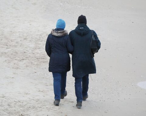 Ein Paar spaziert am Strand, symbolisiert Diskussion über Ehegattenversicherung und Familienpolitik.