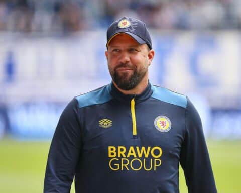 Heiner Backhaus in Fußballkleidung, nachdenklich am Spielfeldrand, symbolisiert Trainerwechsel bei Eintracht Braunschweig.