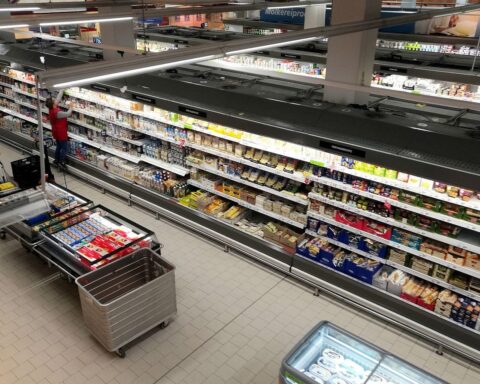 Supermarktregale mit Lebensmitteln, umgeben von Preisschildern und Steuerdiskussionen.