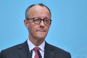 Friedrich Merz spricht auf einer politischen Veranstaltung, umgeben von Banner und interessierten Zuhörern.
