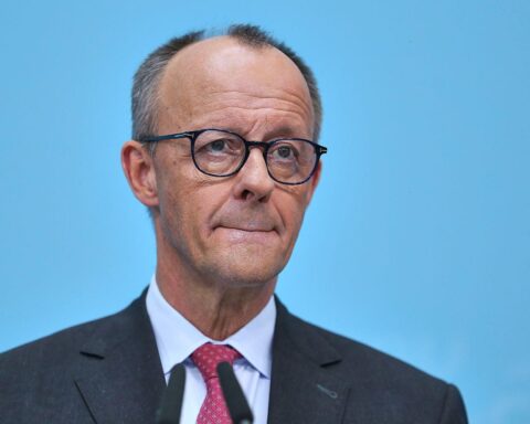 Friedrich Merz spricht auf einer politischen Veranstaltung, umgeben von Banner und interessierten Zuhörern.