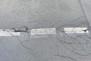 Rissige Fahrbahn mit Schlaglöchern, symbolisiert Frostschäden und notwendige Straßenreparaturen in Hessen.