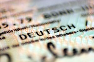 Personalausweis in den Händen eines jungen Menschen mit Migrationshintergrund vor neutralem Hintergrund.