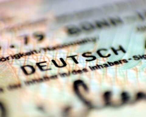 Personalausweis in den Händen eines jungen Menschen mit Migrationshintergrund vor neutralem Hintergrund.