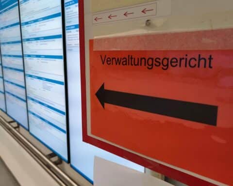 Grafik eines überfüllten Verwaltungsgerichts mit Asylsuchenden und richterlichen Aktenbergen.