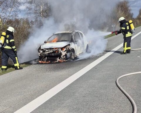 Feuerwehr löscht brennenden Kleinwagen auf Autobahn, starke Rauchentwicklung, Einsatzkräfte mit Atemschutz.