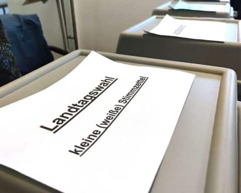 Wahlurnen, Wähler und Stimmzettel symbolisieren die Landtagswahl in Rheinland-Pfalz und politische Unsicherheit.