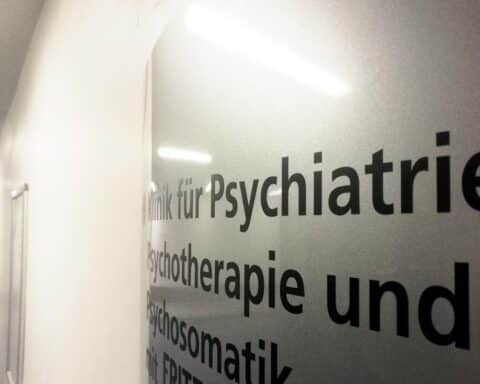 Demonstration gegen Psychotherapie-Honorarkürzungen mit Plakaten und Teilnehmern vor Klinik.