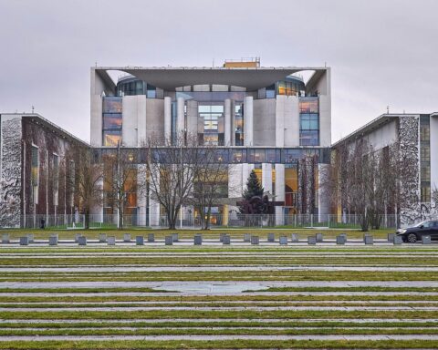 Bild des Bundeskanzleramts mit politischen Symbolen der Kritik an diplomatischen Beziehungen zu Syrien.