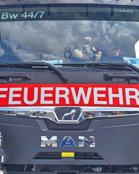 Wagen der Feuerwehr vor Hochhaus, Einsatzkräfte retten verletzte Person aus verrauchter Wohnung.