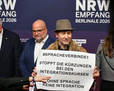 Protestierende Menschen mit Schildern gegen Kürzungen bei Integrationskursen, symbolisieren soziale Ungerechtigkeit.