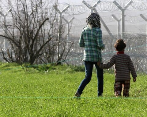 Flüchtlinge stehen vor einem Grenzzaun, symbolisieren Migrationskrise und Sicherheitsbedenken Europas.