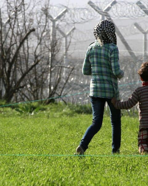 Flüchtlinge stehen vor einem Grenzzaun, symbolisieren Migrationskrise und Sicherheitsbedenken Europas.