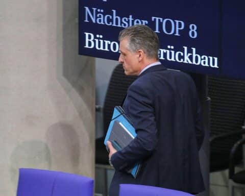 Ein besorgter Geschäftsmann betrachtet Bürokratie-Aushänge an einer Anzeigetafel in Köln.