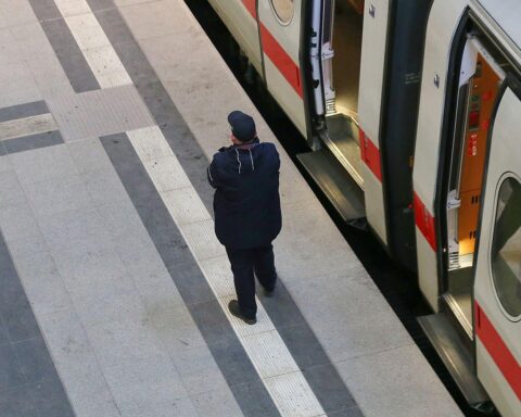 Ein Schaffner der Deutschen Bahn überprüft Fahrgäste am Gleis, symbolisiert Zuverlässigkeit im Schienenverkehr.