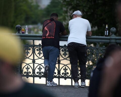 Zwei Männer auf Brücke im Sonnenlicht, umgeben von mildem Wetter und aufziehendem Nebel.