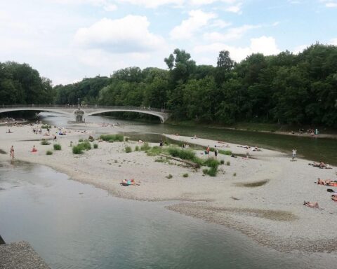 Sonniger Isarstrand in München, mit strahlendem Himmel und entspannenden Menschen am Ufer.