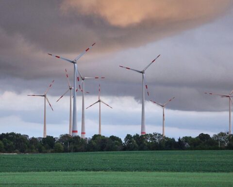 Windräder unter wechselhaftem Himmel, umgeben von Wolken und Anzeichen von Gewittern.