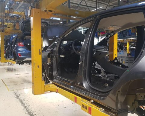 Schemenhafte Fabrik mit Autos, leere Arbeitsplätze, ernste Stimmung; sinkende Jobangebote in der Autoindustrie.