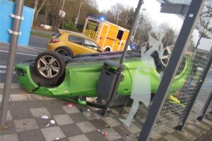Auto auf dem Dach in Bushaltestelle, Unfallstelle mit Polizei und beschädigten Fahrzeugen.