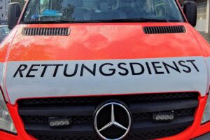 Unfallstelle mit Feuerwehr, Rettungswagen und Elektroauto, umgeben von Einsatzkräften und Absperrungen.