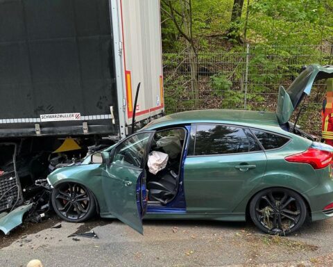 Unfallstelle: Ford Focus unter Sattelauflieger, Polizei und Rettungswagen vor Ort.