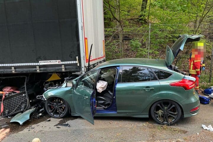 Unfallstelle: Ford Focus unter Sattelauflieger, Polizei und Rettungswagen vor Ort.