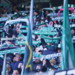 Zufriedene Fans von Werder Bremen und Hamburg beim Fußballspiel, umgeben von Polizeipräsenz.