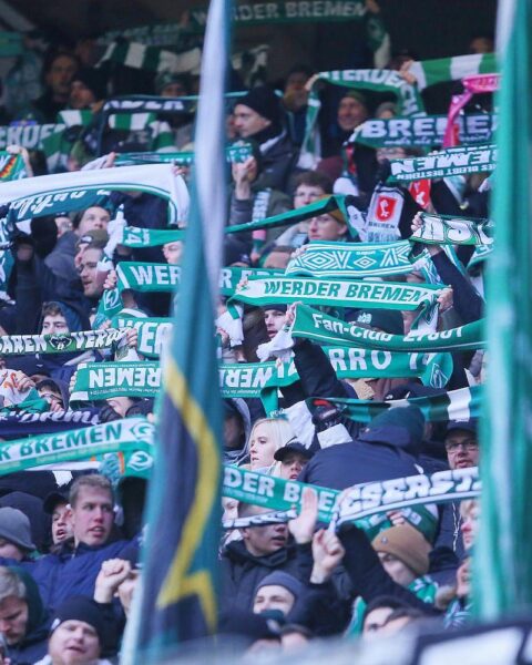 Zufriedene Fans von Werder Bremen und Hamburg beim Fußballspiel, umgeben von Polizeipräsenz.