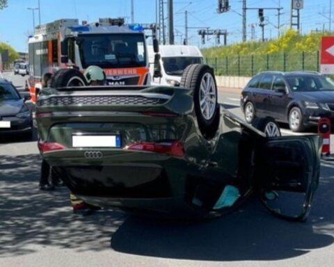 Verunfallter Audi auf dem Dach, Baum, und beschädigter VW im Hintergrund, Polizei im Einsatz.