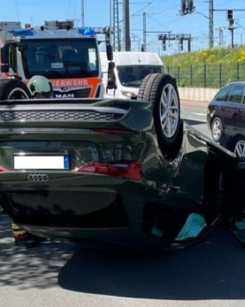 Verunfallter Audi auf dem Dach, Baum, und beschädigter VW im Hintergrund, Polizei im Einsatz.