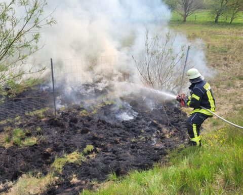 Feuerwehr löscht Böschungsbrand, große Rauchwolke über Grasland, Fahrzeuge und Einsatzkräfte vor Ort.