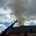 Feuerwehrleute löschen Brand in Einfamilienhaus, starke Rauchentwicklung und Schäden am Dachstuhl sichtbar.