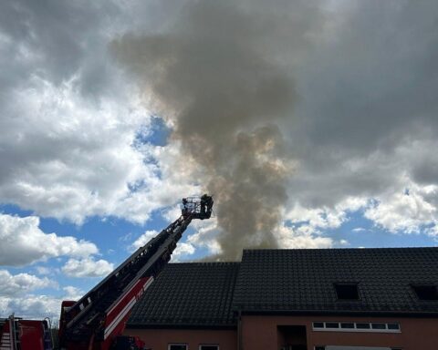 Feuerwehrleute löschen Brand in Einfamilienhaus, starke Rauchentwicklung und Schäden am Dachstuhl sichtbar.