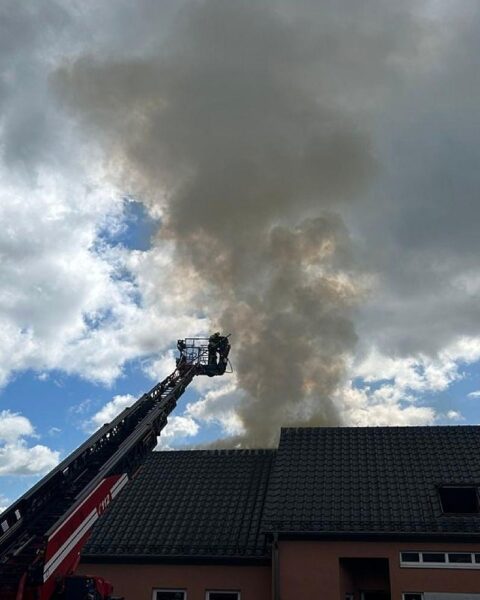 Feuerwehrleute löschen Brand in Einfamilienhaus, starke Rauchentwicklung und Schäden am Dachstuhl sichtbar.