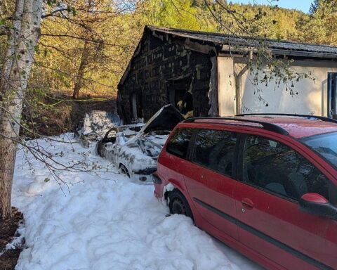 Brennende Autos, Feuerwehr im Einsatz, angrenzendes Wohngebäude betroffen, Rauch und Flammen sichtbar.