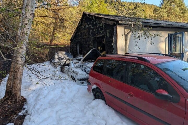 Brennende Autos, Feuerwehr im Einsatz, angrenzendes Wohngebäude betroffen, Rauch und Flammen sichtbar.