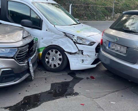 Unfallstelle mit beschädigten Fahrzeugen, Polizei und Rettungskräften, leicht verletzte Personen werden versorgt.