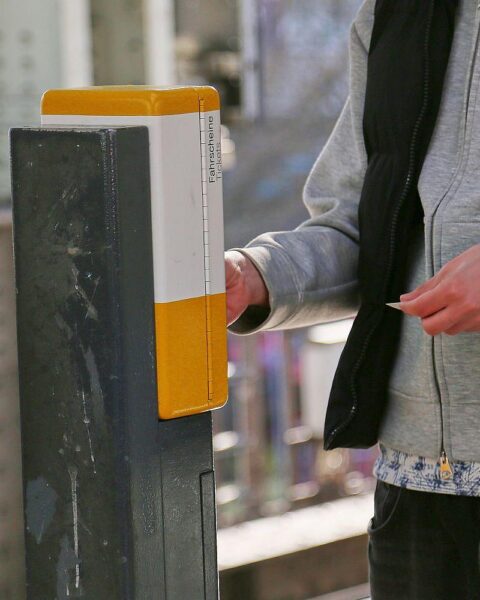 Ein Fahrgast stempelt eine Fahrkarte in einem öffentlichen Verkehrsmittel, symbolisiert Ticketkontrolle.