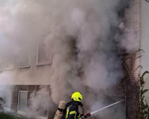 Feuerwehrleute löschen Brand in Betriebsgebäude; schwarzer Rauch steigt empor, Einsatzkräfte aktiv.