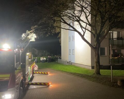 Anwohner versammeln sich vor einem Wohnhaus, Feuerwehrleute löschen Brand im Badezimmer.