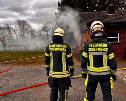 Einsatzkräfte der Feuerwehr löschen Zimmerbrand, starke Rauchentwicklung sichtbar, Gebäude nicht mehr bewohnbar.