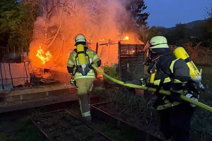 Feuerwehr löscht Brand in Gartenhütte; Rauchwolke und Einsatzkräfte im Einsatz sichtbar.