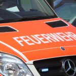 Feuerwehr-Rettungswagen vor einem Wohnhaus, Einsatzkräfte bei Rauchentwicklung, besorgte Anwohner.