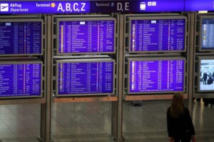 Frau vor Informationstafel am Frankfurter Flughafen, symbolisiert steigende Passagierzahlen und neues Terminal.